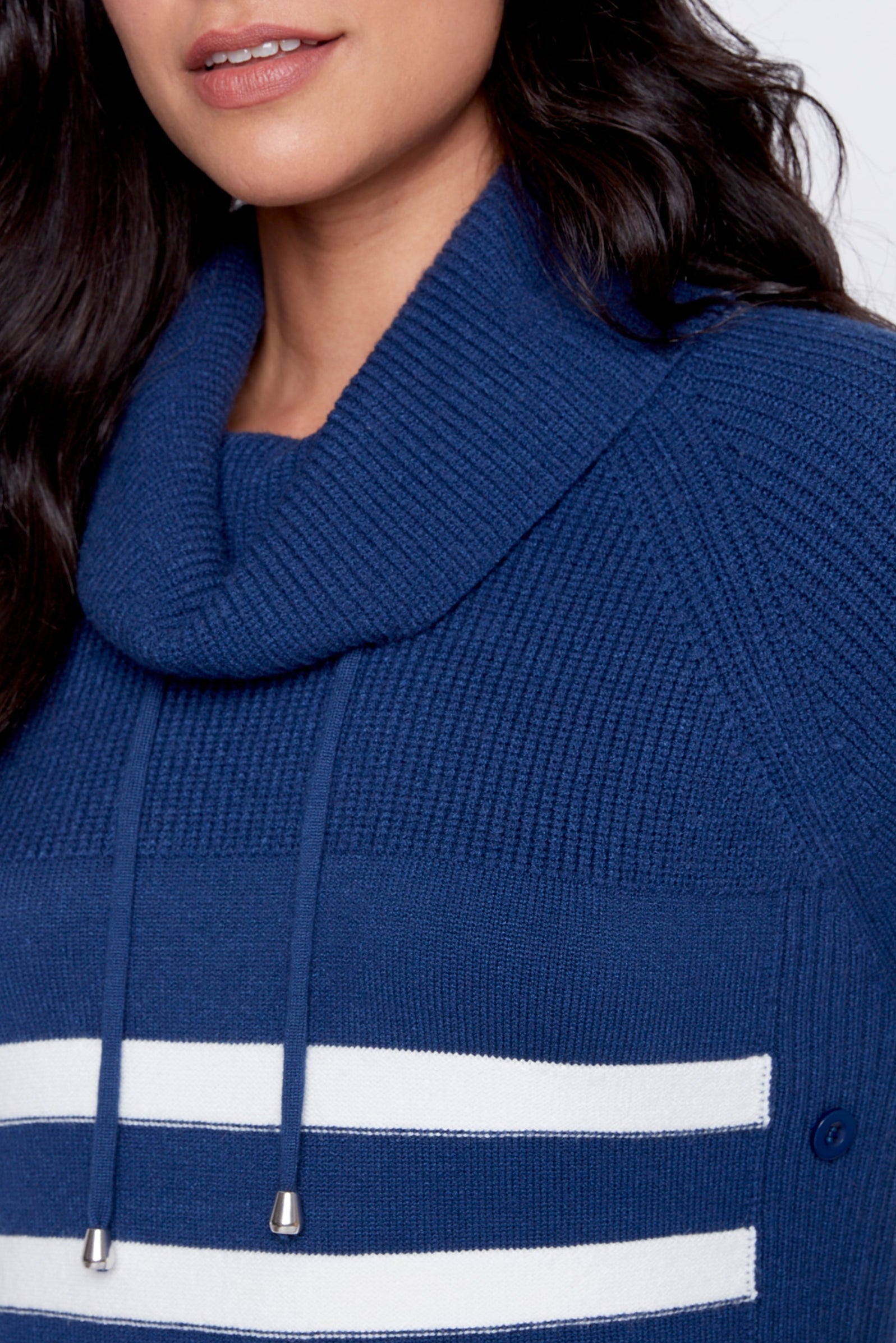 Woman wearing a blue and white striped sweater with a cowl neck on a plain background